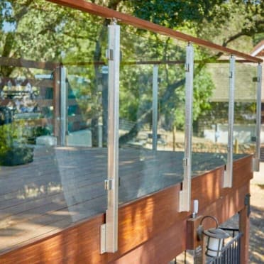 Brushed stainless fascia-mounted posts with glass panels and a wood cap rail along a wooden deck edge.