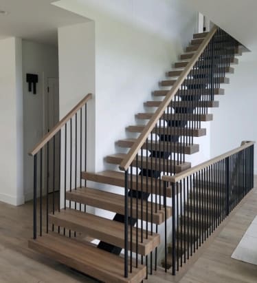 Wood floating treads on a black mono stringer with black vertical balusters and wood handrails climb a white stairwell.