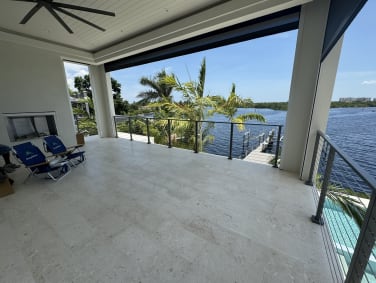 Slim gray rod railing edges a covered stone lanai overlooking a waterway lined with palms.