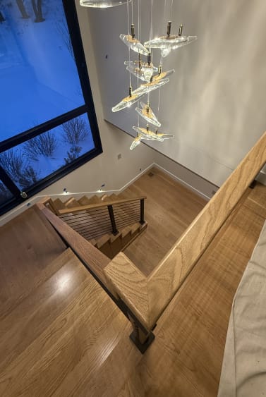 Looking down an oak stair and landing with onyx black rod railing beneath a glass chandelier