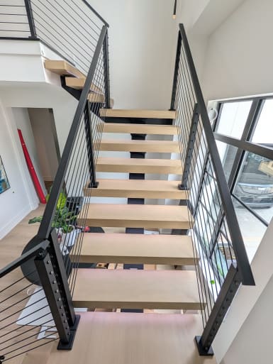 Straight run of white oak floating treads flanked by black-post cable railings with LED glow at the base.