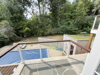 White-post cable railing with a dark wood top rail edges a flagstone terrace above a pool