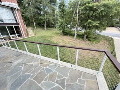White-post cable railing with a dark wood rail edges a flagstone terrace beside a brick home
