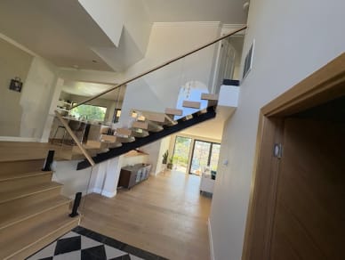 White oak floating stair with glass on talons and a wood handrail overlooking an open living room