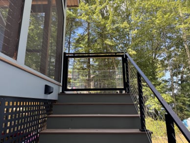 Black cable railing climbs exterior stairs to a jet black rod-infill gate