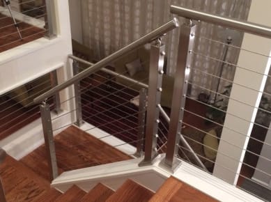 Brushed stainless posts and round handrail with cable infill follow a wood stair turning at a landing.