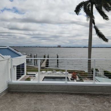 Bright white posts with horizontal rods line a rooftop overlooking a bay, dock and pool.