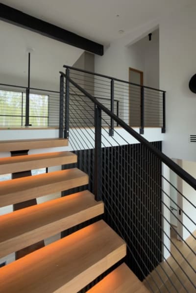 Close view of LED-lit white oak floating treads beside black rod railing