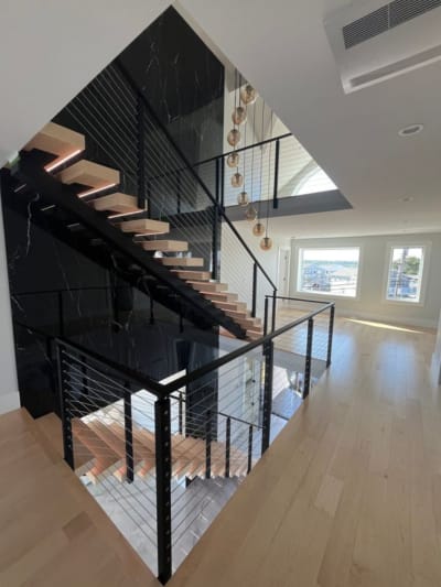 Two flights of LED-lit maple floating treads with black cable railing around an open stairwell