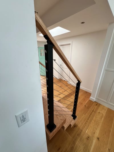 Black cable railing and oak handrail at the base of a floating stair