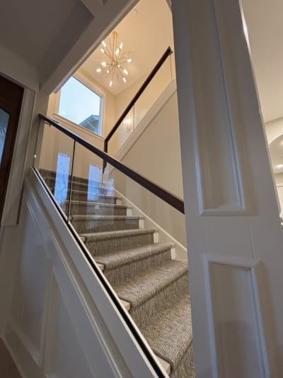 Frameless base rail glass with a dark walnut cap along a stair with a woven runner and white trim