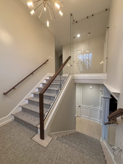 Frameless base rail glass with a dark walnut cap along a stair with a woven runner and white trim