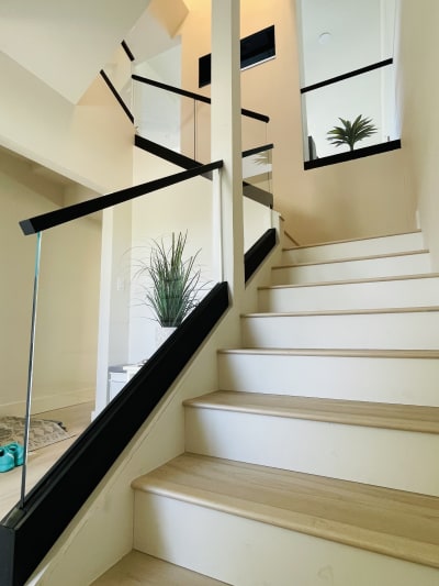 A white oak stair rises beside frameless glass railing set in a black channel with a black handrail.