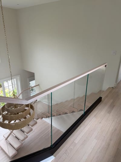 Looking down past a base-rail glass guard with oak handrail onto white-oak floating treads and a woven pendant.