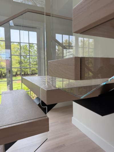 Close detail of thick white-oak floating treads and frameless glass panels against windows.