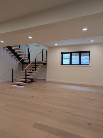 White oak mono switchback stair with cable railing set in a large open room with light oak floors.