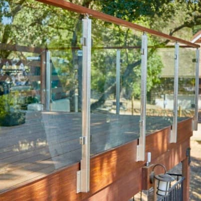 Brushed stainless fascia-mounted posts with glass panels and a wood cap rail along a wooden deck edge.