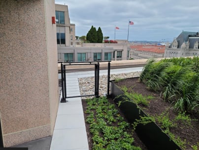 Black cable railing with a gate on its own hinge post beside planters on a city rooftop terrace.