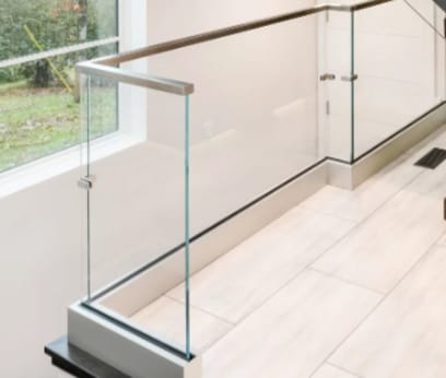 Clear glass railing in a white base rail with a metal top cap wraps a stair opening by a window.