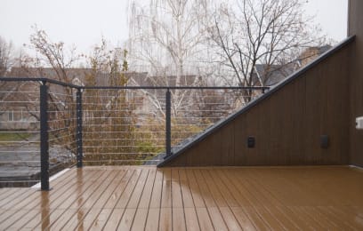 Black cable railing on a composite deck changes height beside an angled wood-clad wall.
