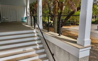 Black cable railing between white porch columns with a matching black handrail down wide white steps.