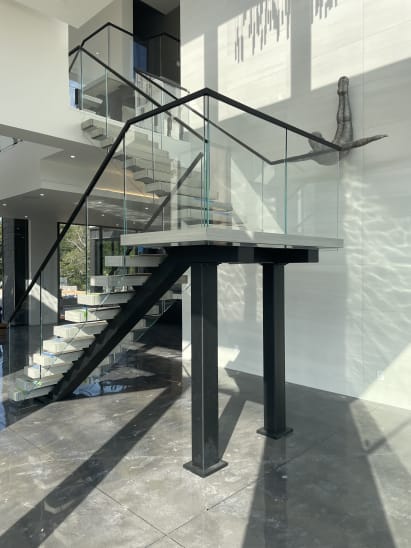 Sunlit floating switchback stair with frameless glass and black handrail on twin steel columns