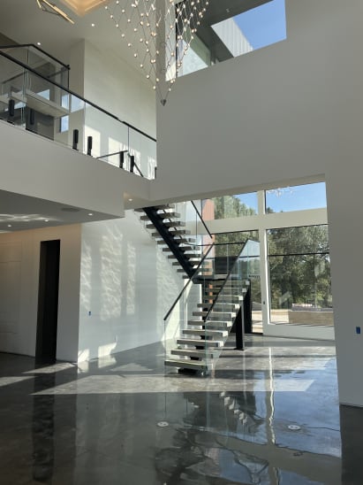 Floating stair rising beside floor-to-ceiling windows, with a glass balcony railing above