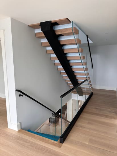 Light oak treads on a black mono stringer with frameless glass running from floor toward the ceiling.