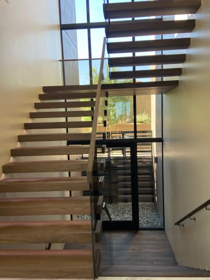 Walnut cantilevered treads with frameless glass climb beside a tall window wall and door to a courtyard.