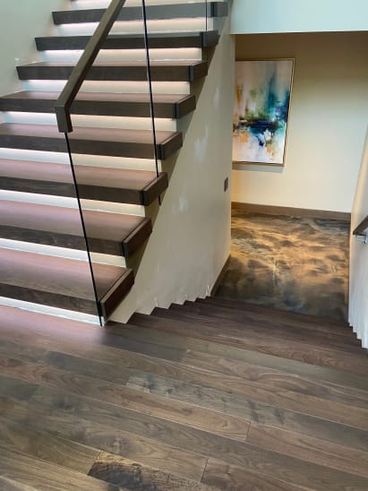 Walnut cantilever treads with LED under-lighting and frameless glass descend to a walnut landing.