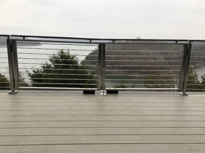 Stainless-framed cable double gate set into a cable railing on a gray deck above a lake.