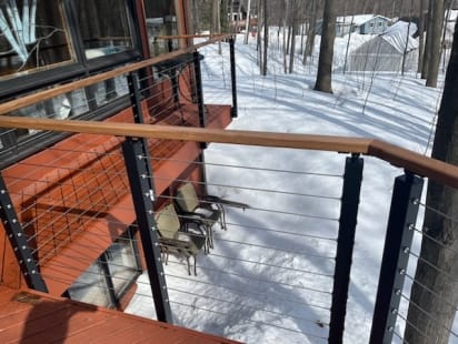 Black slim posts and wood cap cable railing along a red deck above a snowy yard.