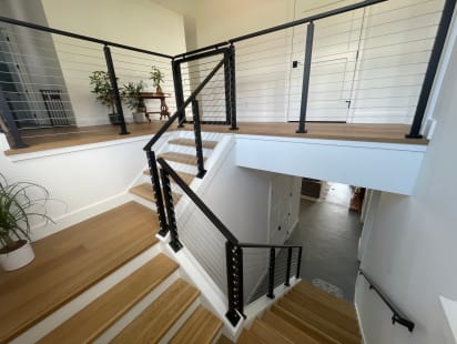 Black cable railing follows a white oak split-level stair and landing in a bright white home.
