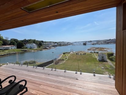 Frameless laminated glass on stainless talons edges a hardwood deck overlooking a harbor and green lawn.
