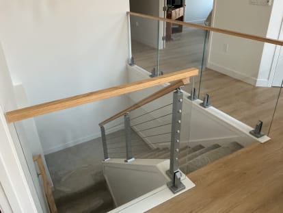 Frameless glass on surface-mount talons paired with a cable railing section and oak handrail around a stair opening.