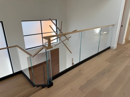 Frameless glass in a black floor channel with a light wood handrail around a stair opening with oak floors.