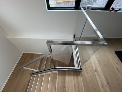 Frameless glass with a brushed stainless cap wraps an open-riser stair opening