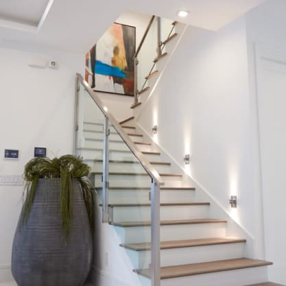 Brushed stainless posts and glass panels follow a white stair with oak treads and wall-mounted step lights.