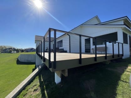 Black slim side-mount cable railing with double corner posts wraps a raised deck on a white farmhouse.