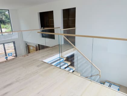 Frameless glass and wood handrail guard a stair opening, with floating treads below