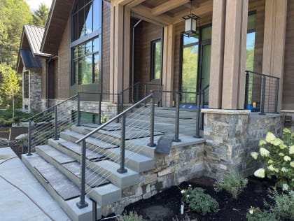 Black cable railing lines wide stone entry steps up to a timber porch with hydrangeas