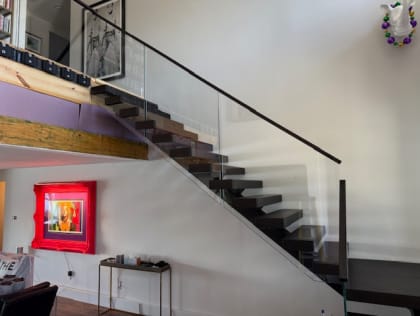 Espresso floating treads with frameless glass on standoff pins and a black handrail beside bold art