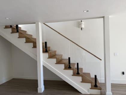 An oak staircase with glass panels on black ascend talons and a slim wood handrail in a white room.