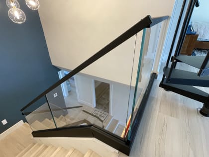 Frameless glass panels in a black channel with a black handrail descend a light oak stair.