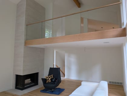 Frameless glass with a wood cap rail and no visible hardware edges a loft above a living room with a corner fireplace.