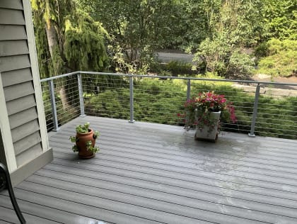 A gray composite deck with flower pots edged by gray cable railing against lush shrubs.