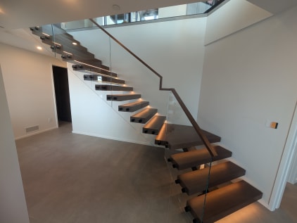 Walnut floating stair with glowing LED treads and frameless standoff glass with walnut handrail
