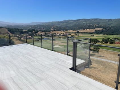 Dark-post glass railing edges a tile terrace overlooking a golf course and rolling hills.