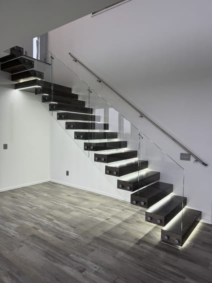 Dark cantilever floating stair with glowing LED treads, standoff-pin glass and stainless handrail