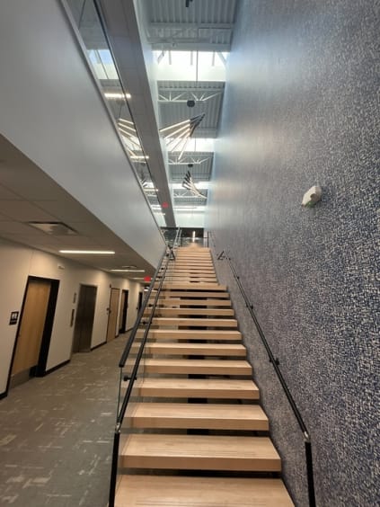 Long oak floating stair with glass railing and black handrail in a commercial office atrium.